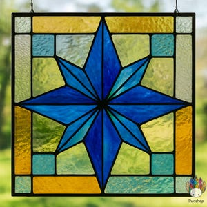 May include: Stained glass window panel featuring a vibrant blue starburst design. The star is surrounded by geometric shapes in shades of yellow, green, and blue, all framed by a black border. The panel is designed to hang.