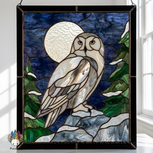 Könnte beinhalten: Buntglasfenster mit einer Schnee-Eule auf einem schneebedeckten Felsen, vor einem Nachthimmel mit Vollmond. Die Eule hat weiße und graue Federn, mit grünen Bäumen auf beiden Seiten. Das Fenster ist schwarz gerahmt.