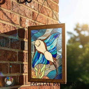 Op de afbeelding: Gebrandschilderd glaspaneel met een manta rog in blauw, wit en bruin, gevat in een houten frame. Het paneel hangt aan een ketting tegen een bakstenen muur. De tekst "DIGITAL PATTERN" is zichtbaar.