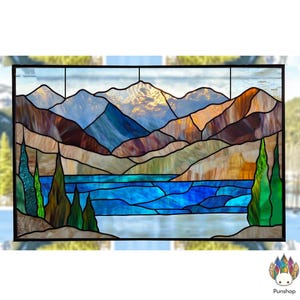 Könnte beinhalten: Ein Buntglasfenster, das eine Bergkette mit einem See im Vordergrund zeigt. Die Berge sind eine Mischung aus Braun, Blau und Lila, mit einem goldenen Sonnenuntergangsglanz. Der See ist leuchtend blau mit weißen Wellen. Das Fenster ist schwarz gerahmt.