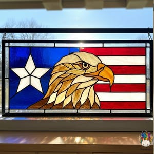 May include: Stained glass panel featuring an American bald eagle and the American flag. The eagle is depicted in shades of brown, tan, and gold, with a yellow beak. The background includes a blue field with a white star and red and white stripes.