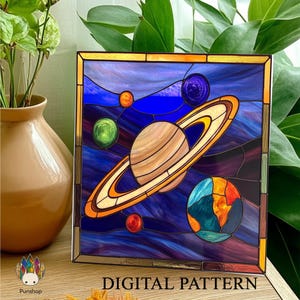 Puede incluir: Un diseño de vitral que representa un sistema solar colorido con planetas, estrellas y un fondo azul. El diseño incluye un planeta grande con anillos, un planeta más pequeño con una superficie verde y un planeta azul con una superficie roja y amarilla. El diseño está enmarcado en un marco dorado.