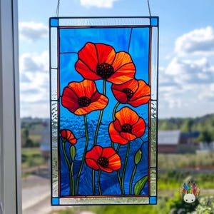 Könnte beinhalten: Ein Bleiglasfenster mit fünf roten Mohnblumen mit blauem und grünem Laub vor blauem Hintergrund.