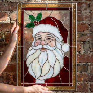 May include: A rectangular stained glass panel featuring a portrait of Santa Claus with a white beard, mustache, and red hat. The design includes green holly leaves with red berries at the top corner, all framed by a border of amber and red glass.