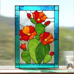 Op de afbeelding: Gebrandschilderd glaspaneel met een cactus met felrode en oranje bloemen en groene bladeren. Het kunstwerk is omlijst met een turkooizen rand. Het ontwerp doet denken aan woestijnflora.