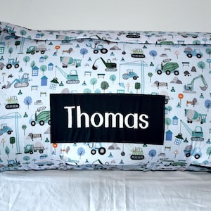May include: A white and blue play mat with a construction vehicle pattern. The mat has a black name tag with the name "Thomas" printed in white.