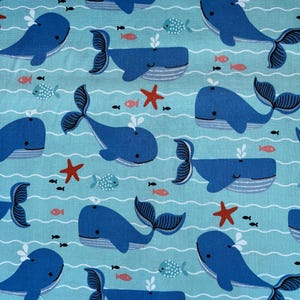 May include: A light blue fabric with a repeating pattern of blue whales, red starfish, and small fish. The whales have dark blue tails and are swimming in wavy lines. The overall theme is nautical.
