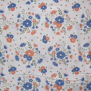 May include: White fabric with a repeating pattern of blue and orange flowers. The flowers are stylized and have a vintage look.