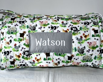 May include: Rectangular pillow with a farm animal print featuring cows, pigs, chickens, and goats on a white background. A gray patch embroidered with the name "Watson" is centered on the pillow. The pillow has a handle.