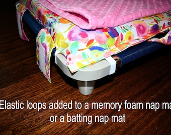 May include: A nap mat with a floral patterned cover and a pink blanket on top. The mat has elastic loops and is on a dark wooden surface. Text on the image reads: "Elastic loops added to a memory foam nap mat or a batting nap mat."
