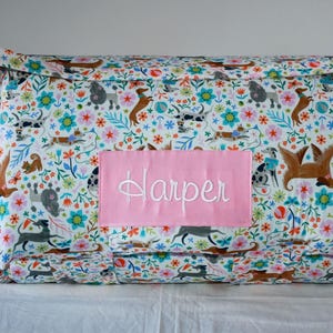 May include: A white and pink personalized nap mat with a floral and dog print. The name "Harper" is embroidered on the mat in white.