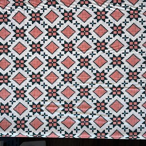 May include: White fabric with a repeating pattern of red and black geometric shapes. The fabric has the text "winterglow" printed on the edge.