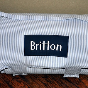 May include: A blue and white striped sleeping mat with a navy blue name tag that says "Britton".