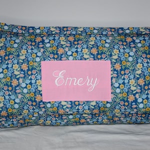 May include: A blue and floral patterned nap mat with a pink personalized patch that says "Emery".