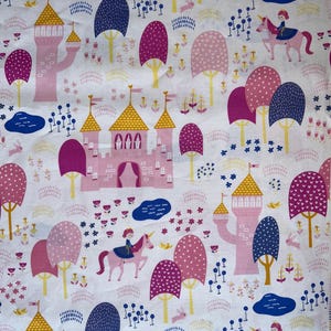 May include: A white fabric with a repeating pattern of pink and blue castles, trees, unicorns, and flowers. The background is white with a subtle pink and blue pattern.