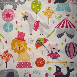 May include: A white fabric with a circus-themed pattern. The design includes cartoon elephants, lions, seals, unicorns, and a circus tent. The color palette features pink, green, orange, and gray elements, with star and balloon motifs.