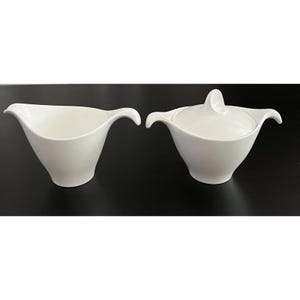 May include: Two-piece white ceramic serving set. The set includes a gravy boat with a curved handle and a covered sugar bowl. Both pieces have a smooth, glossy finish and a minimalist design, suitable for formal dining.