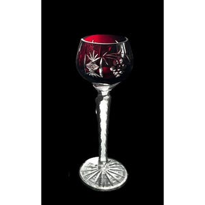 May include: A ruby red wine glass with a clear, faceted stem and base. The bowl features etched starburst and grape cluster designs. The glass is set against a black background, highlighting its elegant form.