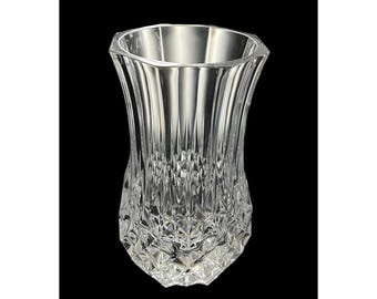 May include: A clear, faceted crystal vase with a flared shape. The vase has a geometric design on the lower portion and vertical lines on the upper portion. The vase is empty and sits against a black background.