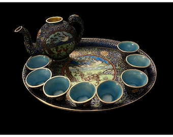 May include: An ornate tea set with a blue and gold color scheme. The set includes a teapot, several small cups, and a serving tray. The tray and teapot are decorated with detailed landscape scenes. The cups have a bright blue interior.
