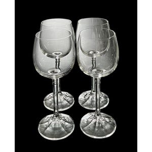 May include: Four clear wine glasses with a classic design. Each glass features a rounded bowl, a slender stem, and a wide, patterned base. The glasses are arranged against a black background, highlighting their transparency and elegant form.