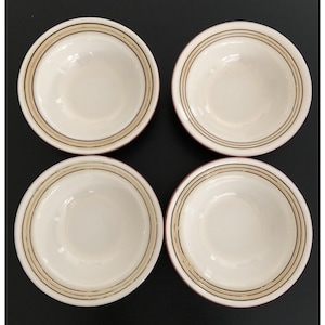 May include: Four off-white ceramic bowls with a brown and black striped design around the rim. The bowls have a red rim and are arranged in a square formation against a black background. These bowls are suitable for serving snacks or small portions.