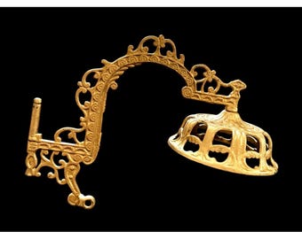 May include: Ornate, gold-colored metal wall sconce with a curved arm and a decorative shade. The sconce features intricate scrollwork and a classic design, perfect for adding a touch of vintage elegance to any space.