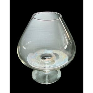 May include: A clear glass vase with a wide, rounded body that tapers to a narrow base. The vase has a flared rim and sits on a small, circular foot. The glass has a slight iridescent quality.