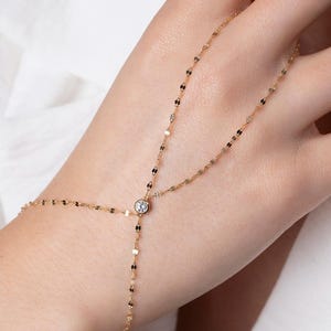 May include: A gold chain bracelet with a single clear gemstone. The bracelet is designed to wrap around the wrist and finger.