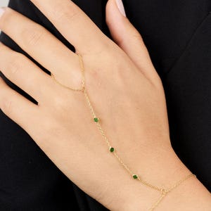 May include: A gold chain bracelet with green gemstones. The bracelet is designed to be worn around the wrist and finger.