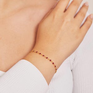 May include: A gold chain bracelet with small, round, red gemstones.