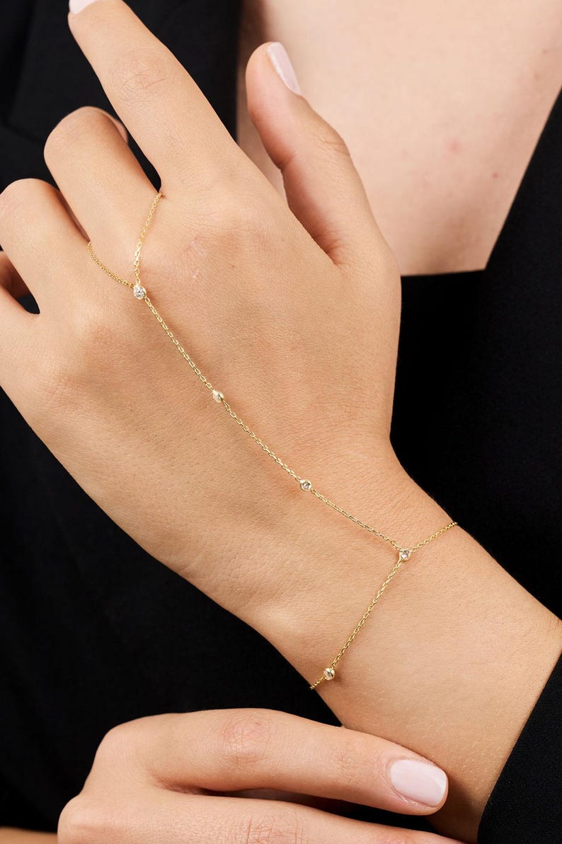 May include: A gold chain bracelet with small diamonds, designed to be worn on the wrist and finger.