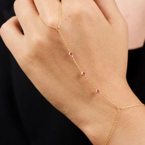 May include: A gold chain bracelet with four small red gemstones. The bracelet is designed to be worn on the wrist and finger.