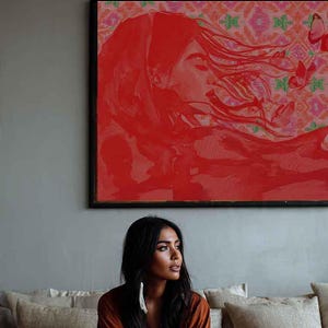 Peut inclure: Une personne vêtue d'une robe couleur rouille est assise sur un canapé beige, avec une peinture rouge au-dessus. La peinture représente un visage de femme et des cheveux flottants. Un vase avec des fleurs séchées est posé sur une table en bois.