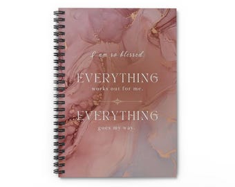 May include: A pink and gold spiral notebook with the text "I am so blessed: EVERYTHING works out for me. EVERYTHING goes my way."