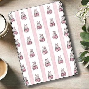 May include: A tablet case featuring a repeating pattern of cartoon bunnies reading books, set against pink vertical stripes on a white background. The case has a clear border and is on a light wood surface.
