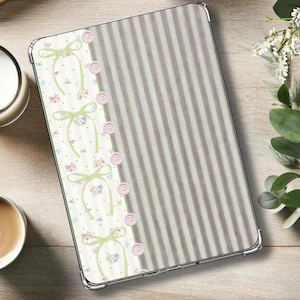 May include: A tablet case with a vertical striped pattern in light gray and white. A decorative side panel features bows, flowers, and pink buttons. The case is on a light wood surface, with a candle and a cup of coffee.