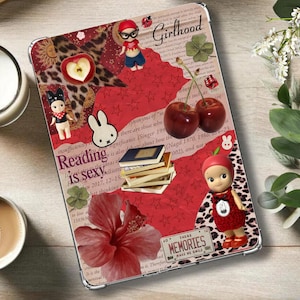 May include: A decorative tablet case with a collage design featuring the text "Girlhood" and "Reading is sexy". The case includes illustrations of cherries, a bunny, a doll, and a hibiscus flower. A cup of coffee and a candle are also visible.