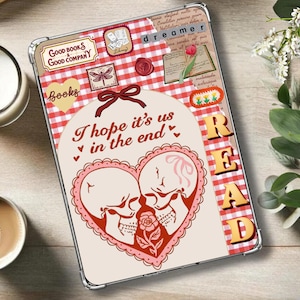May include: A white and red checkered phone case with a pink heart design featuring two skeletons kissing. The text "I hope it's us in the end" is written in black. The word "READ" is written in red and white on the right side of the case.