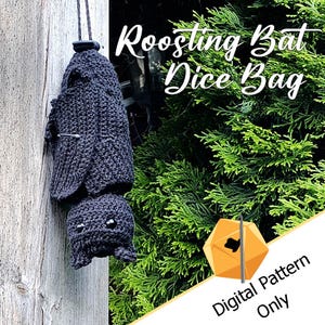 Pode incluir: Uma bolsa para dados em forma de morcego de crochê cinza escuro pendurada por um fio. A bolsa tem uma textura detalhada e olhos pequenos e redondos. O texto "Roosting Bat Dice Bag" é visível. A imagem também inclui o texto "Digital Pattern Only".