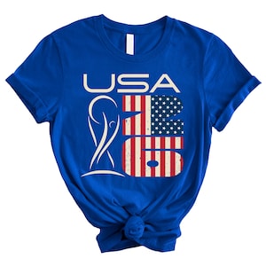 May include: Royal blue t-shirt with the text "USA 26" in white and red, white, and blue. The number "26" is designed with the American flag. The shirt has short sleeves and a crew neck.
