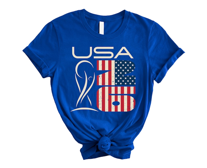 May include: Royal blue t-shirt with the text "USA 26" in white and red, white, and blue. The number "26" is designed with the American flag. The shirt has short sleeves and a crew neck.