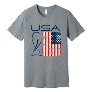 May include: A heather gray t-shirt with the word "USA" in blue, and the numbers "26" in a design resembling the American flag. A blue graphic is on the left side of the shirt.