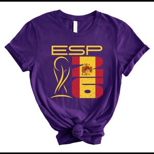 May include: A purple t-shirt with a graphic design featuring the letters "ESP" in yellow, the number "2016" in red and yellow, and a gold emblem. The shirt is knotted at the bottom.