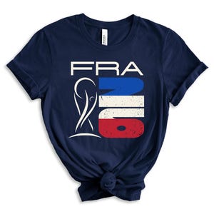 May include: Navy blue t-shirt with a graphic design. The design features the word "FRA" in white, with a stylized image and the word "NO" in the colors of the French flag: blue, white, and red. The shirt is knotted at the bottom.