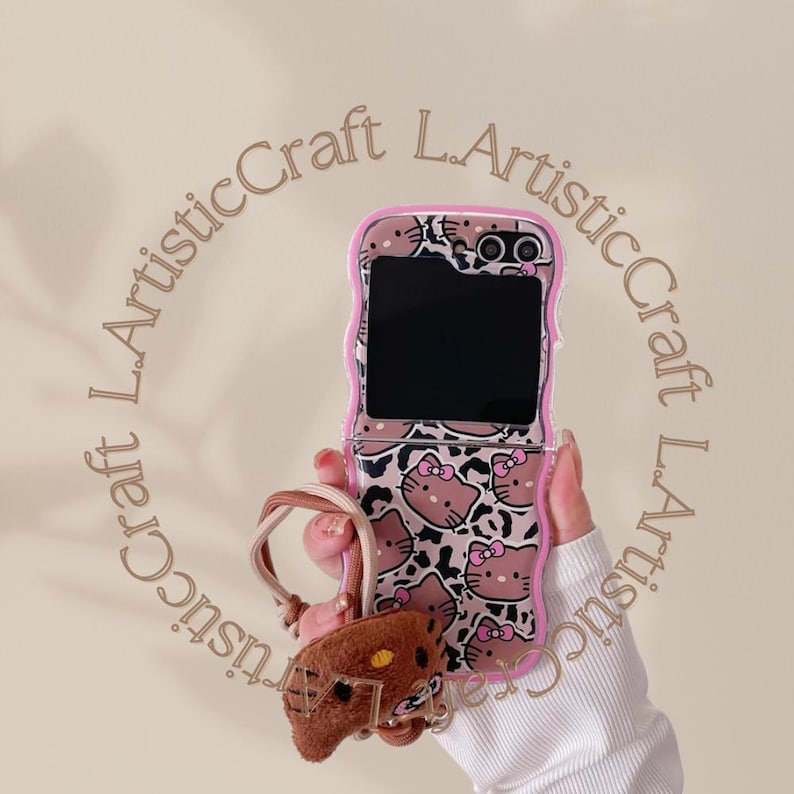 May include: A pink and white Hello Kitty phone case with a flip-up cover. The case has a leopard print design with Hello Kitty faces. The case is attached to a brown Hello Kitty keychain.