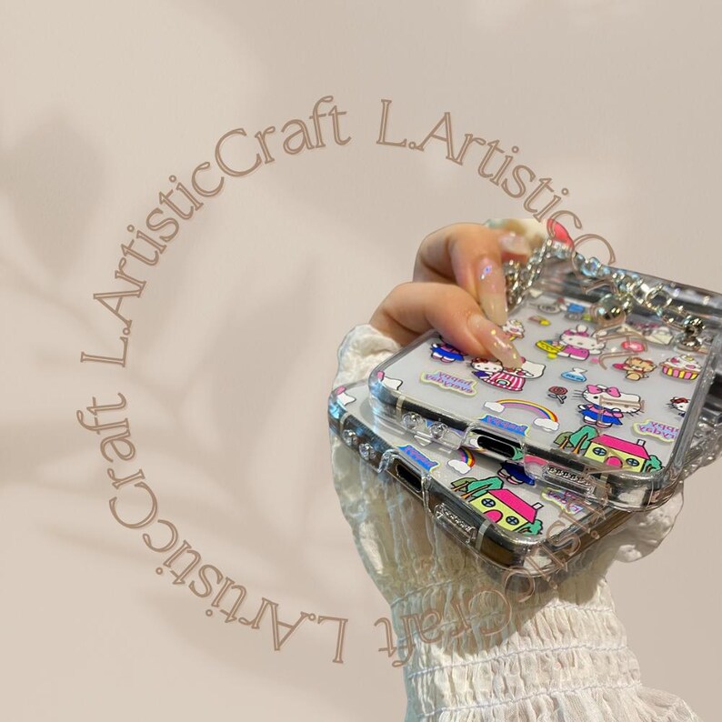 May include: Two clear phone cases with a colorful cartoon design featuring Hello Kitty and other characters. The cases are attached to a silver chain.