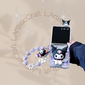 May include: A clear phone case featuring a black and white cartoon character with a skull on its forehead. The case is open, revealing the phone's screen. A matching charm and a beaded bracelet with purple heart-shaped beads are also visible.
