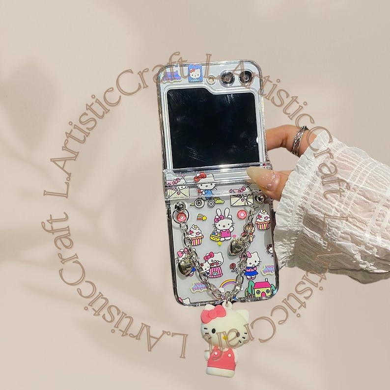 May include: A clear phone case with a Hello Kitty design. The case has a built-in mirror and a chain with a Hello Kitty charm.