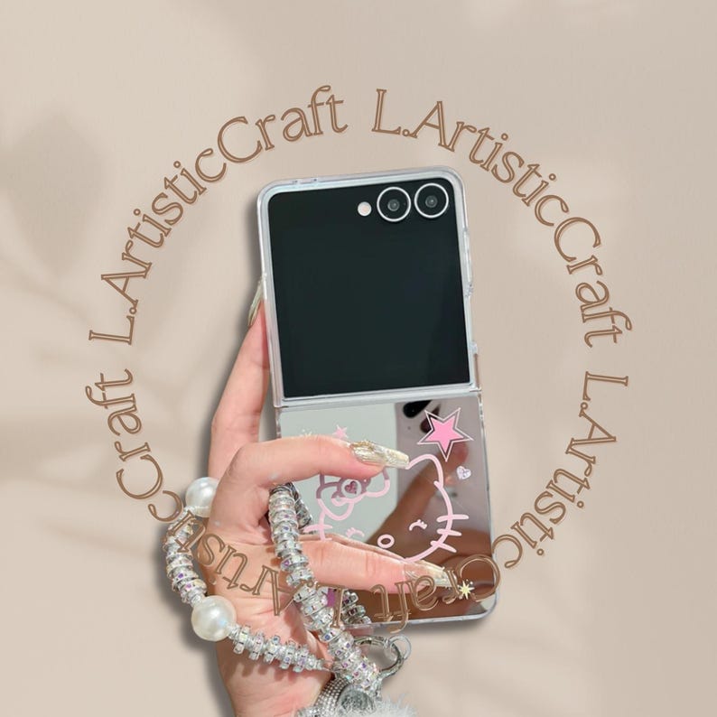 Pu&ograve; includere: Custodia trasparente per telefono con finitura a specchio, con un design rosa di Hello Kitty e una stella. La custodia &egrave; tenuta in mano, con un cinturino da polso di perle e strass. Lo schermo del telefono &egrave; nero.